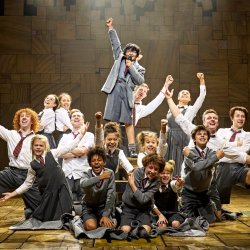 The cast of Matilda The Musical pose at the end of Revolting Children with their arms in the air